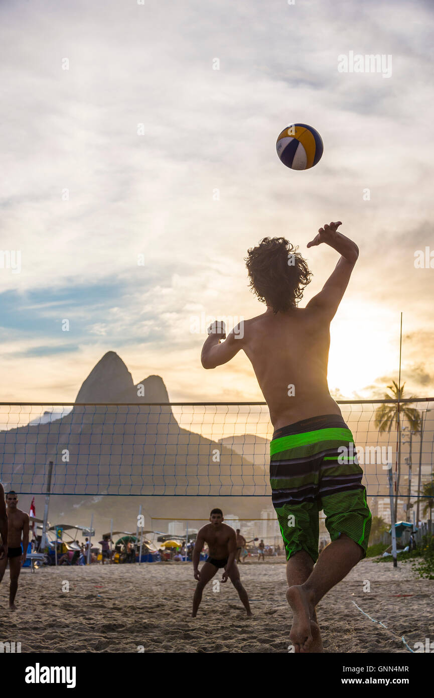 RIO DE JANEIRO - MARCH 20, 2016: Young Brazilians play beach volleyball against a sunset silhouette of Ipanema Beach. Stock Photo