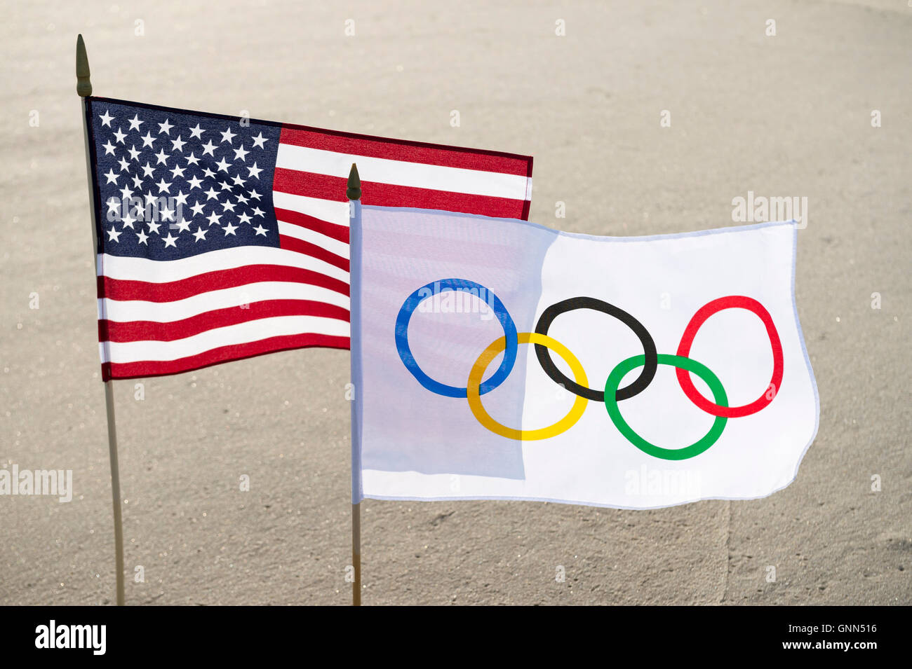 RIO DE JANEIRO - MARCH 24, 2016: Olympic and American flags stand fluttering in smooth sand on the beach. Stock Photo