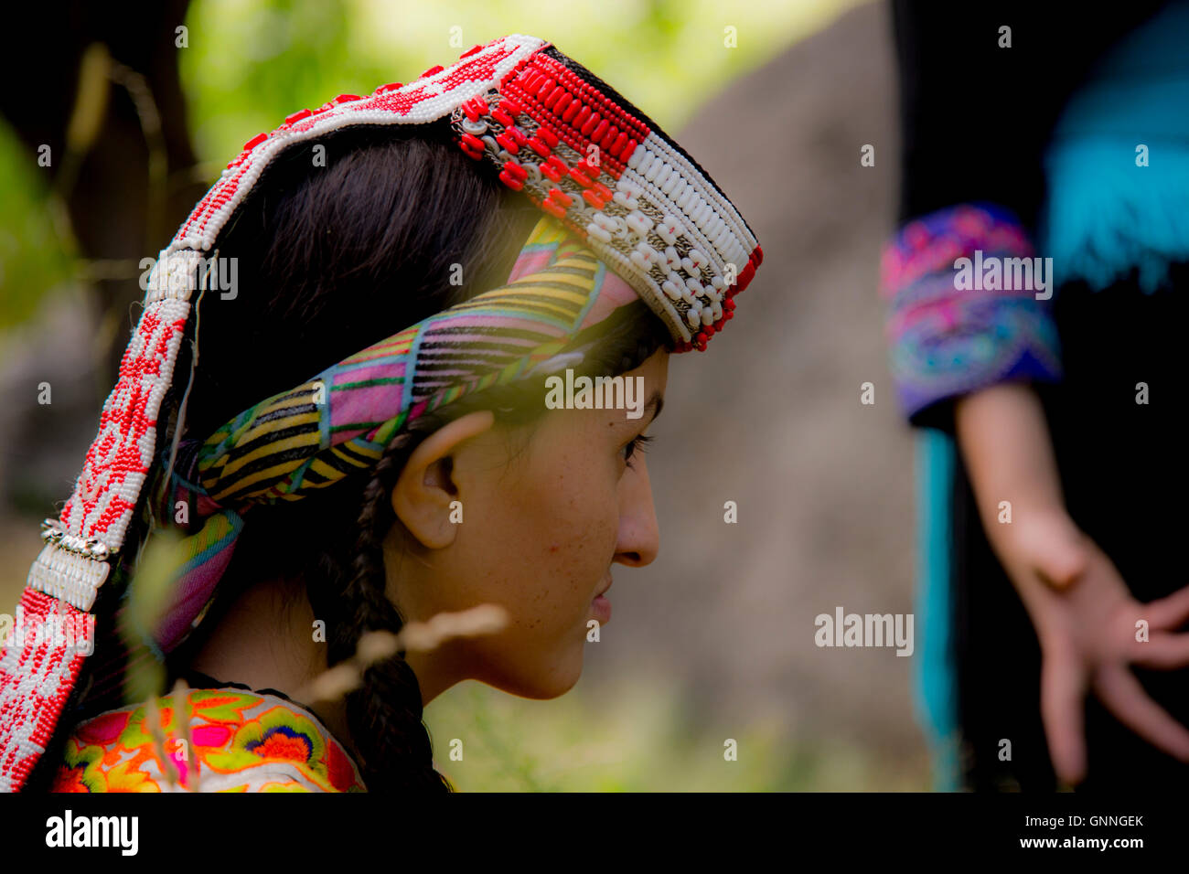 A pretty young Kalasha girl sits in a field of grass in Kalash Valley, Chitral, Pakistan. Stock Photo