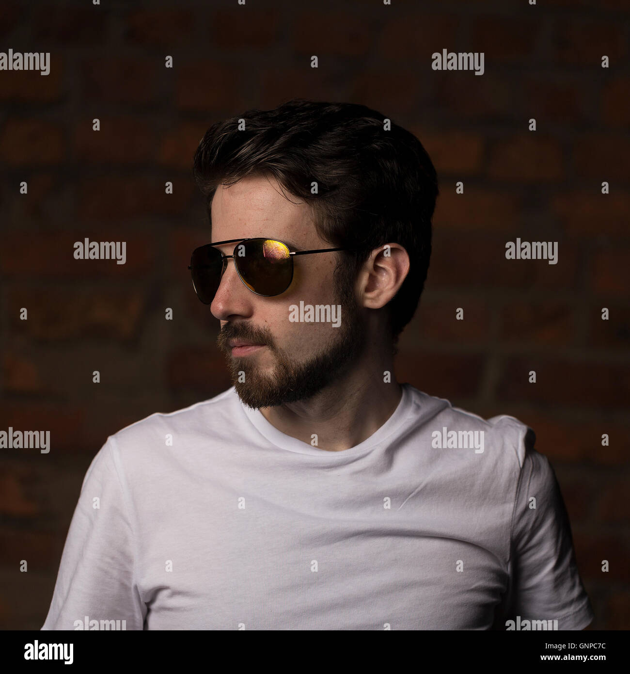 Male model with groomed beard wearing white tee and aviators reflecting red orange yellow sunset light Stock Photo