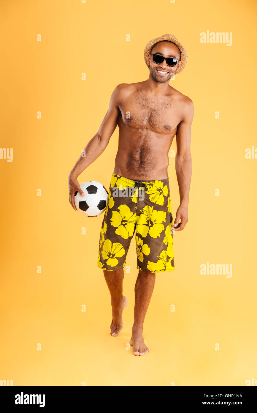 Full length portrait of a young man holding a beach ball isolated on orange background Stock Photo