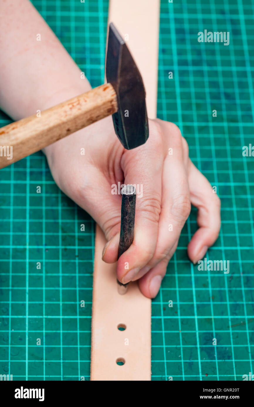 punching holes in leather belt with steel hole punch and hammer on selfhealing mat Stock Photo