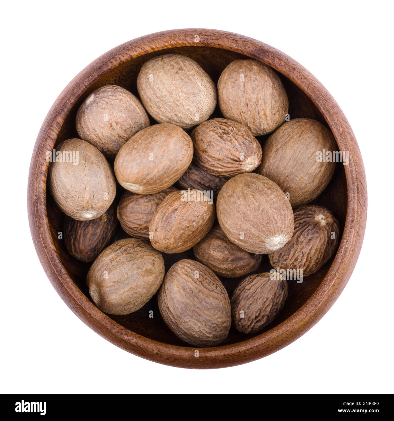 Nutmegs in a wooden bowl on white background. Myristica fragrans, also called pala, an edible brown and egg-shaped seed. Stock Photo