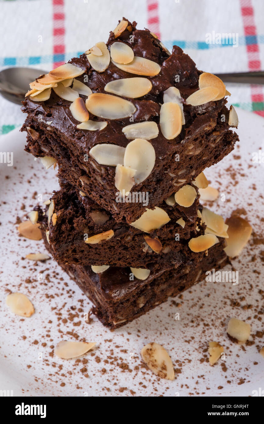 stack of sweet dark brownies with almond slices on white plate Stock ...