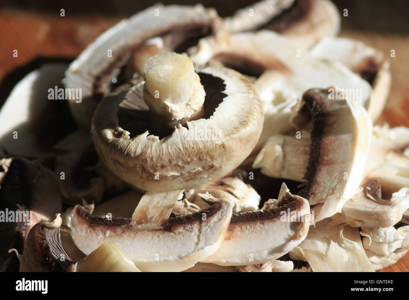 Food preparation - white mushrooms on wooden kitchen worktop waiting to be cooked. Close up of mushroom gills. Stock Photo