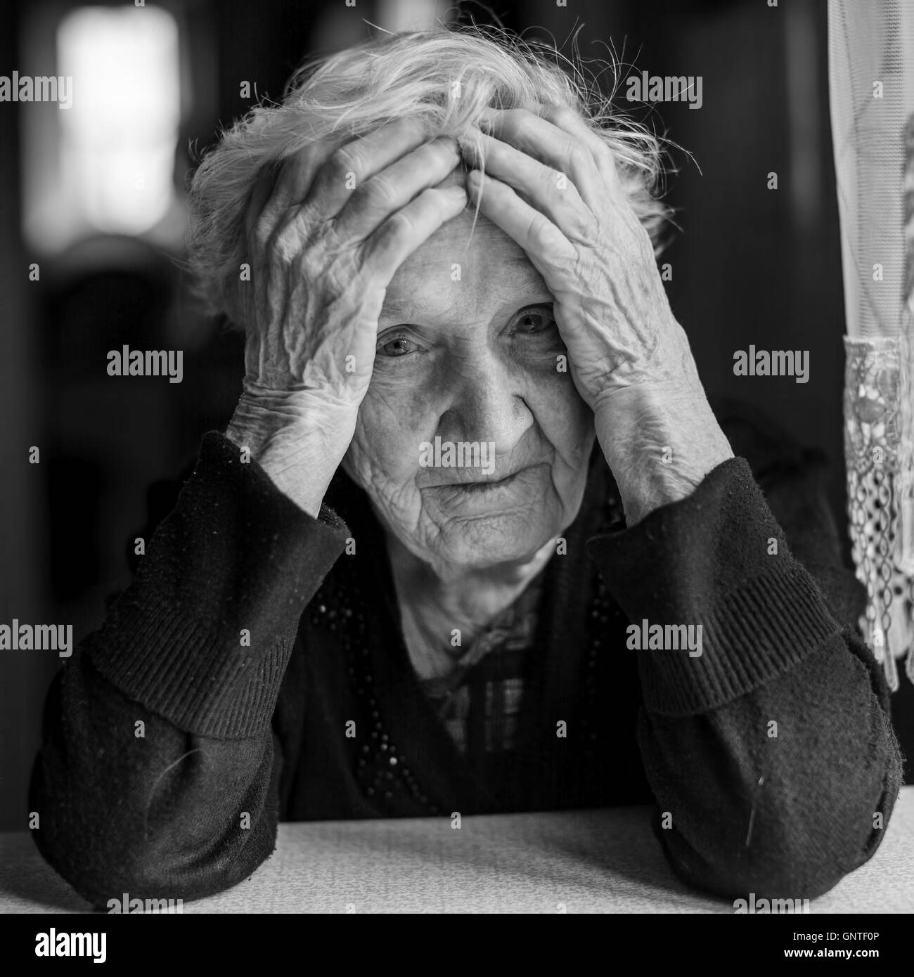 Sad elderly woman holds hands a head. Black and white photo. Stock Photo