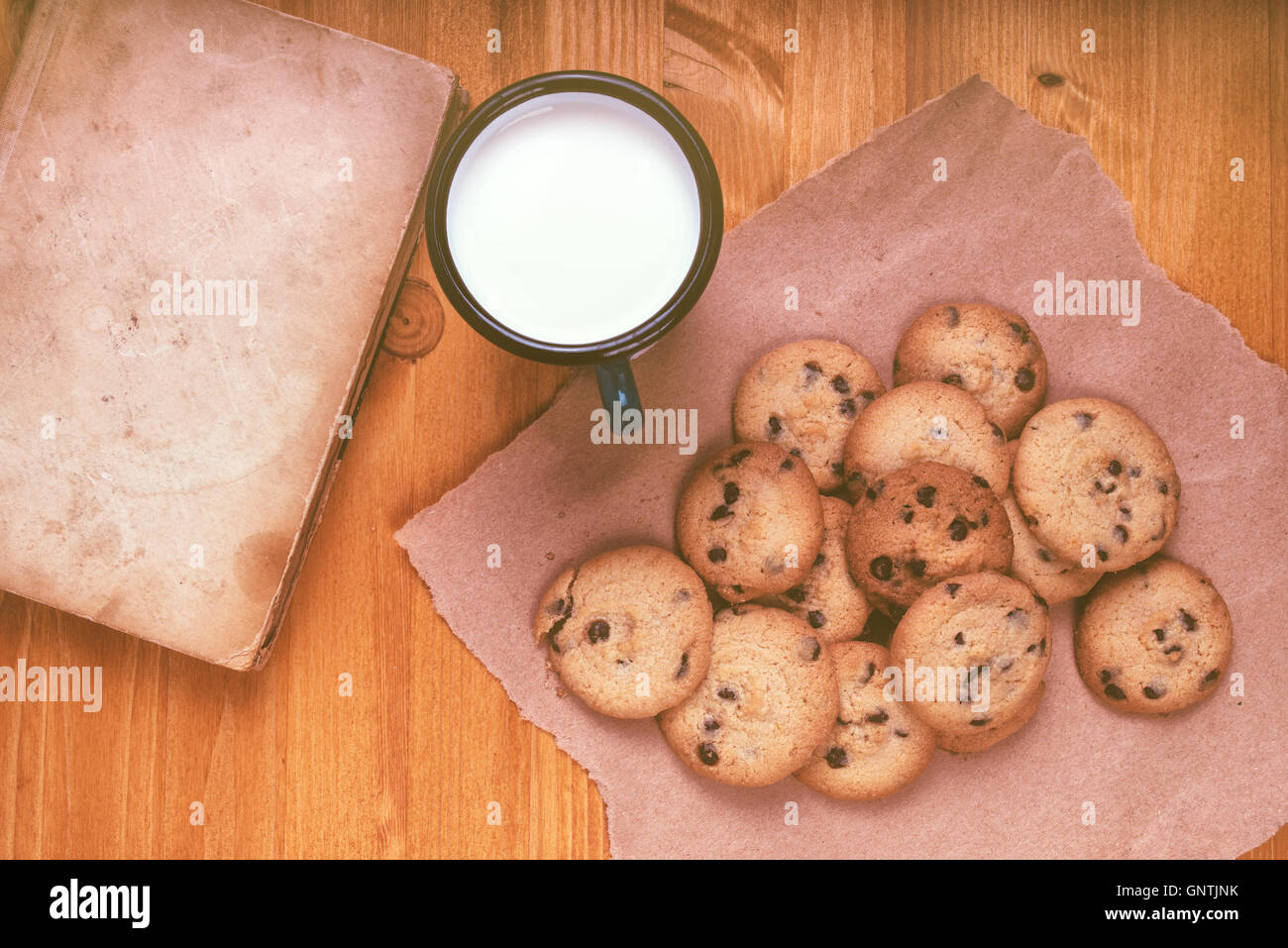 Homemade chocolate chip cookies, milk cup and vintage book on rustic wooden table, top view Stock Photo