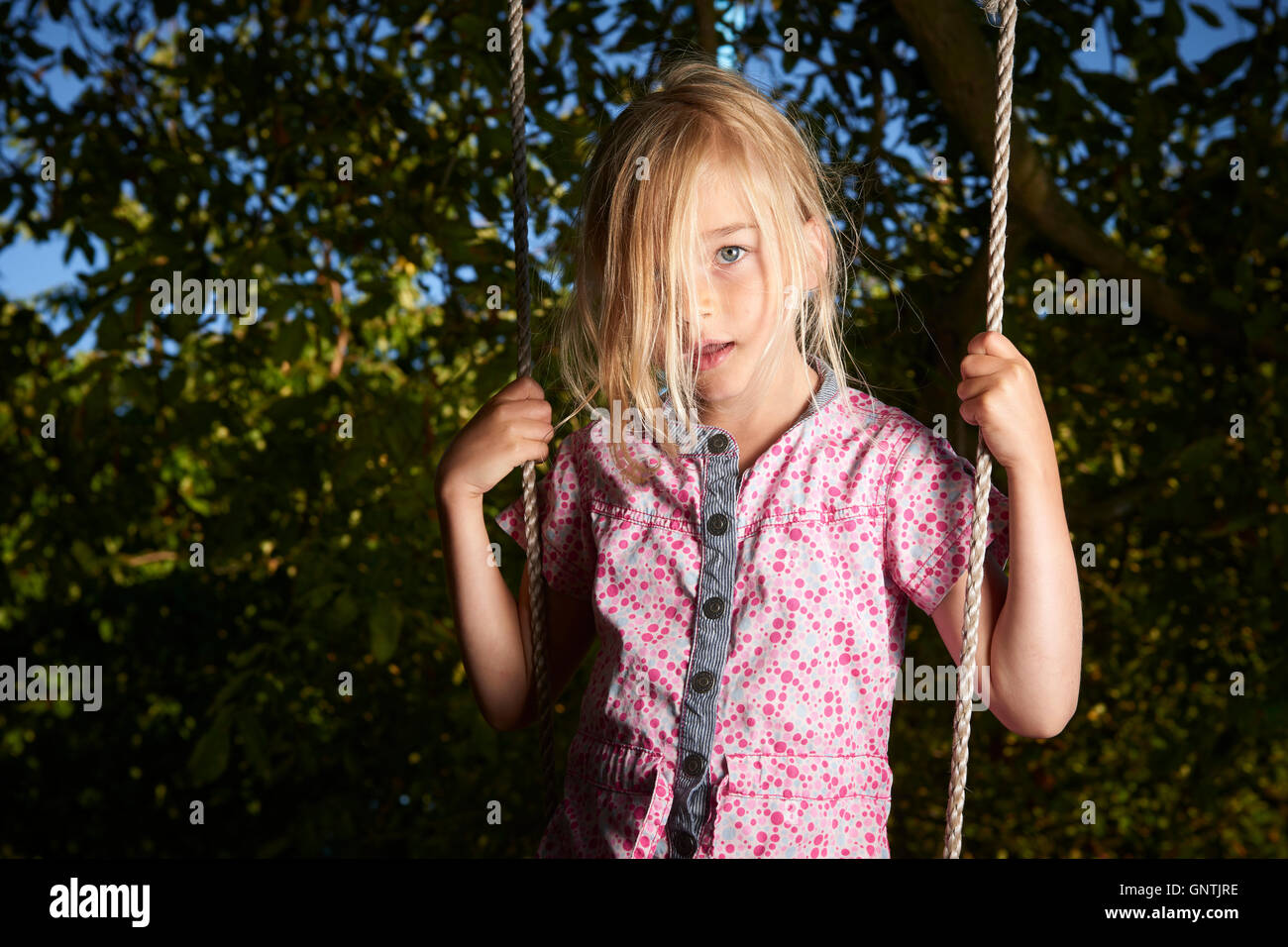 Child blond sad girl standing on swing. Stock Photo