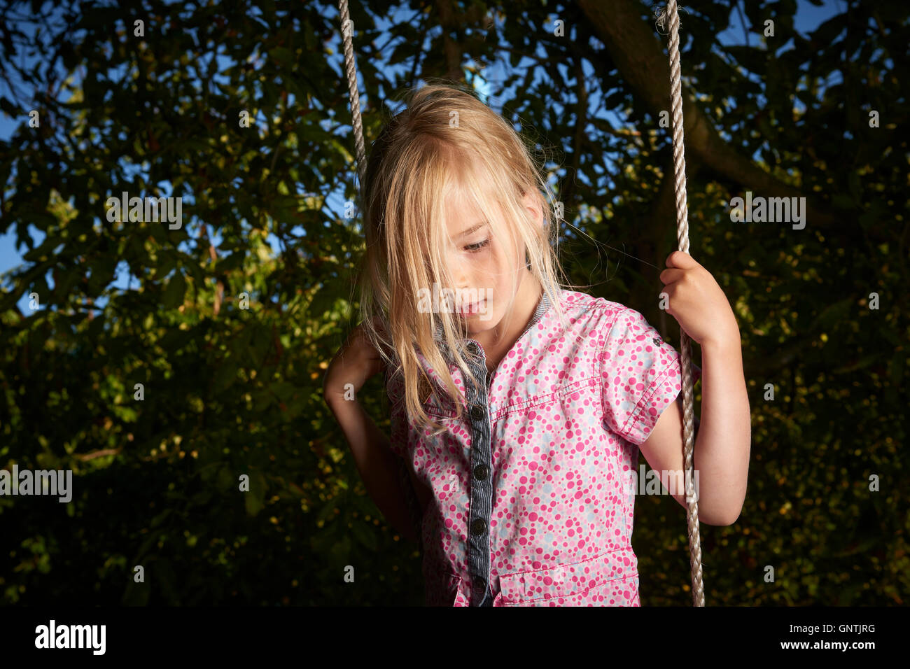 Child blond sad girl standing on swing. Stock Photo