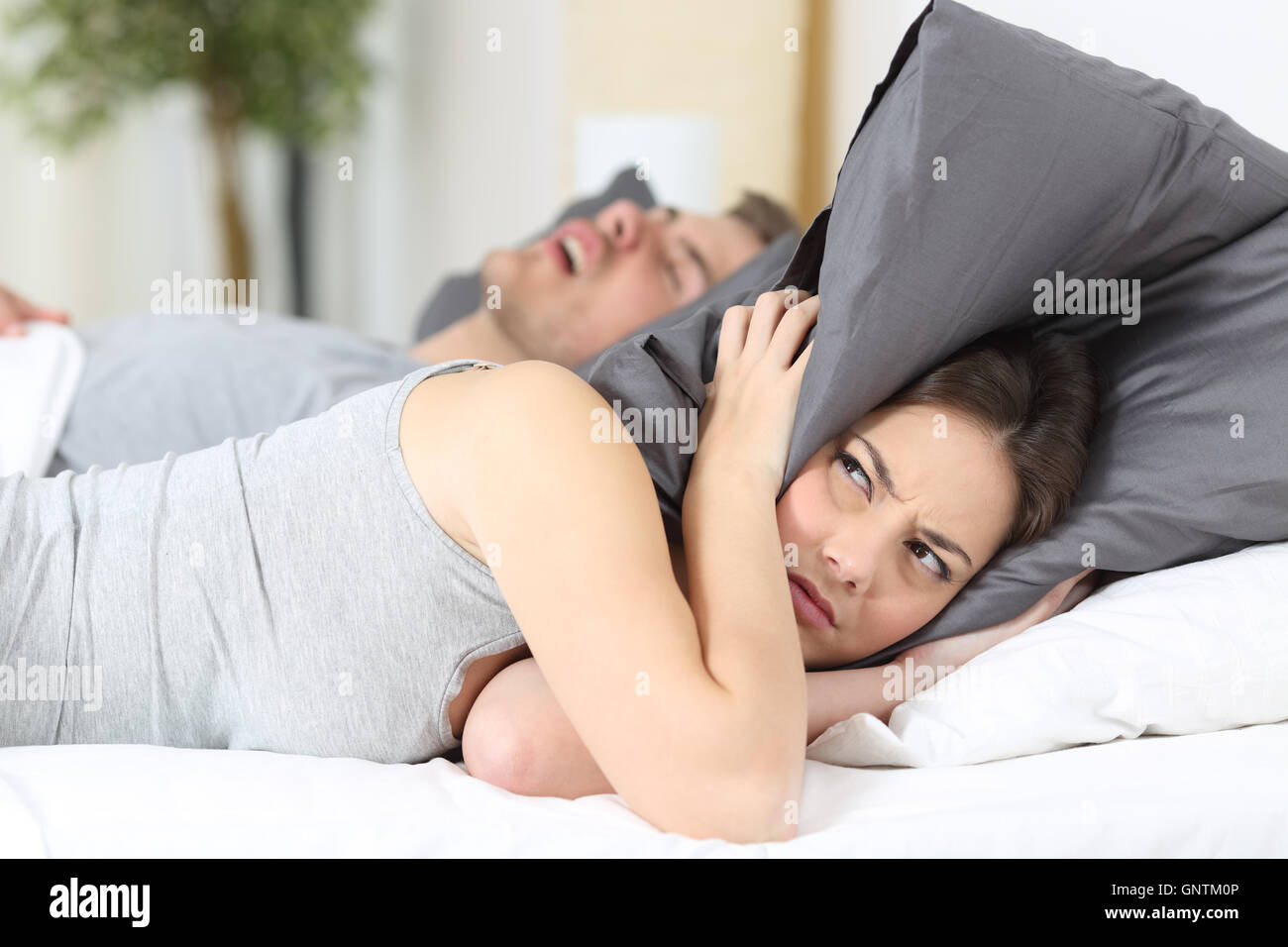 Man snoring while his wife is covering ears with the pillow Stock Photo