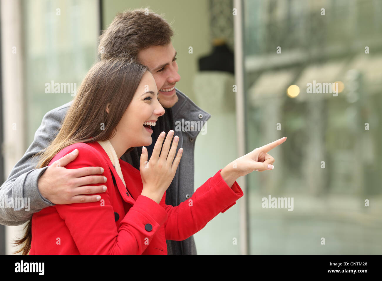 Excited fashion couple shopping and watching in a storefront in a town street Stock Photo