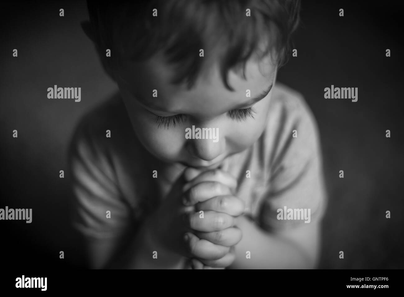 A cute young boy praying with hands clasped, in black and white. Stock Photo