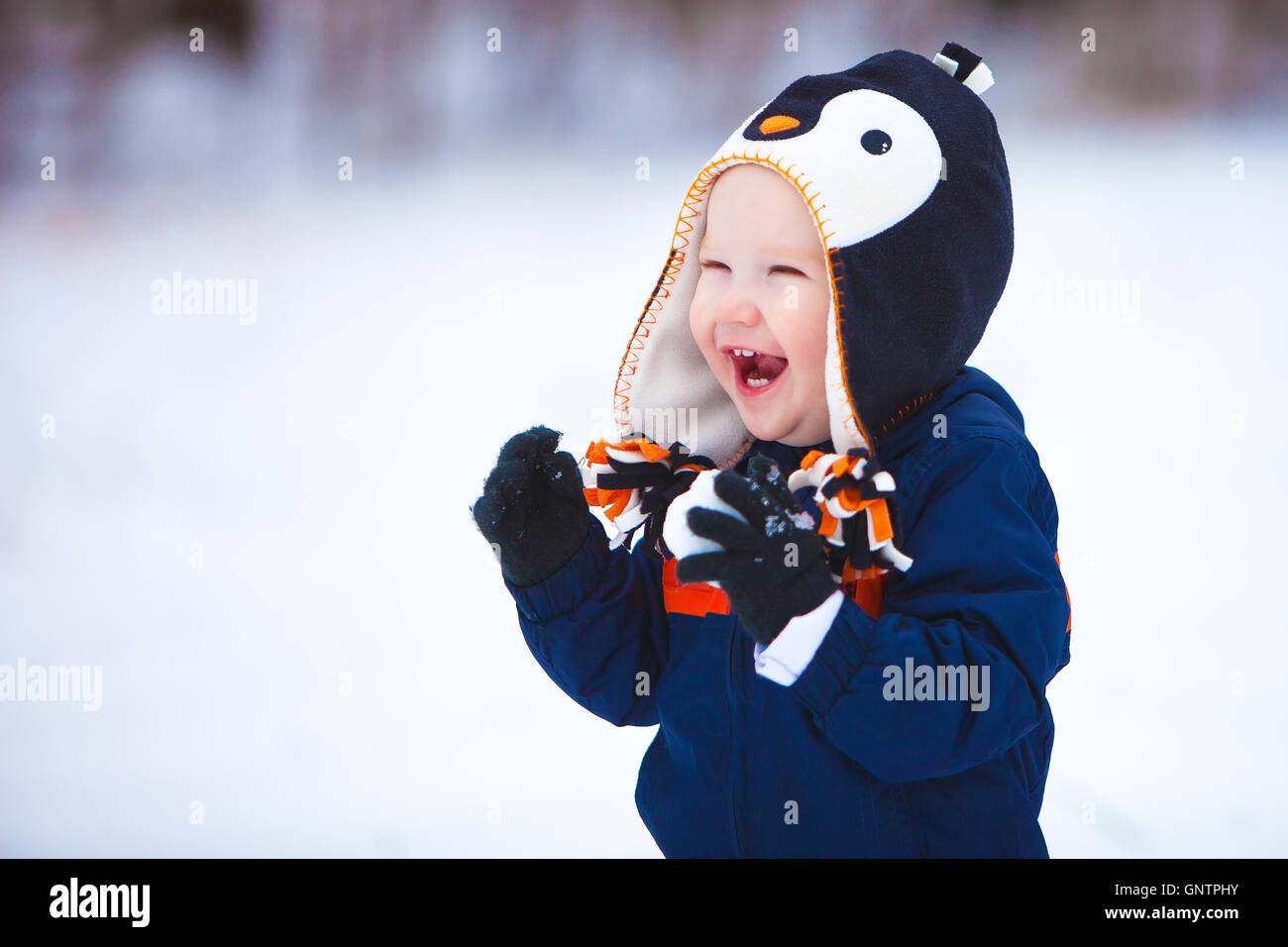 A young boy wearing a winter coat and hat laughs as he plays in the snow. Stock Photo