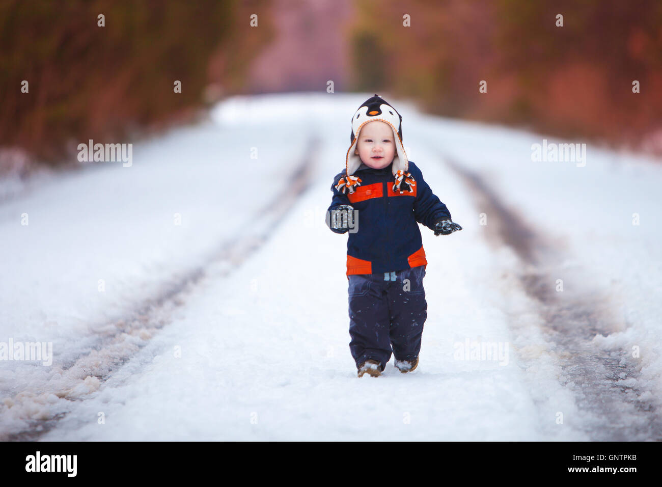 A young boy wearing a winter coat and had smiles as he walks down a snow covered road. Stock Photo