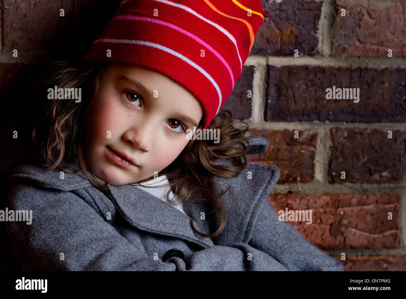 Portrait of a beautiful young child with attitude leaning against a brick wall Stock Photo