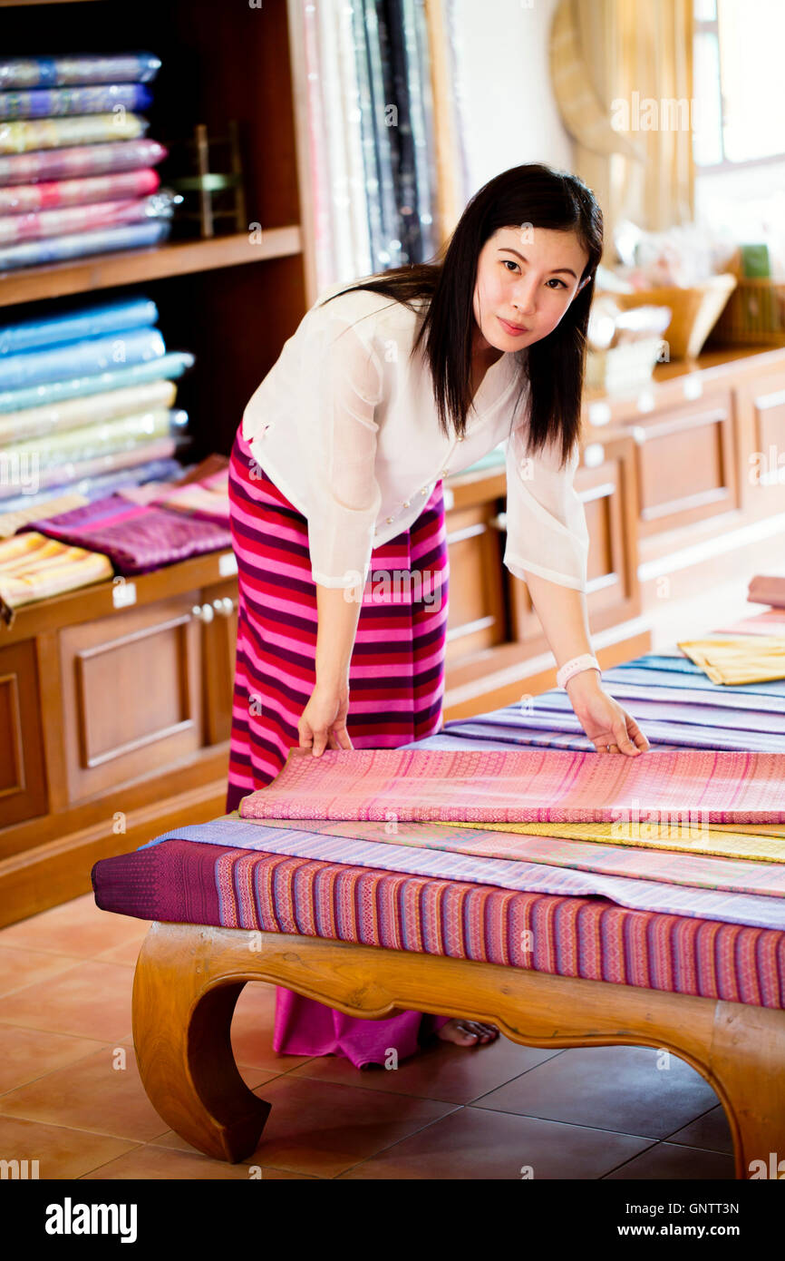 Attendant selling traditional Thai clothing including sinh skirts, Chut Thai & Pha Kung, in a silk weaving shop in Lamphun, North Thailand Stock Photo