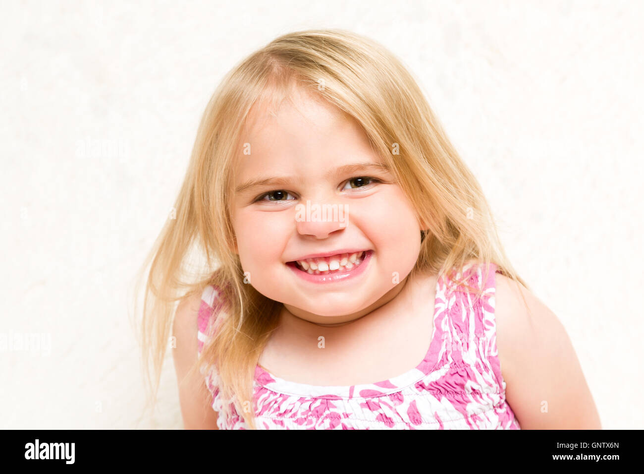 Closeup Portrait of Beautiful Toddler Girl Grinning Cheekily on Neutral Background Stock Photo