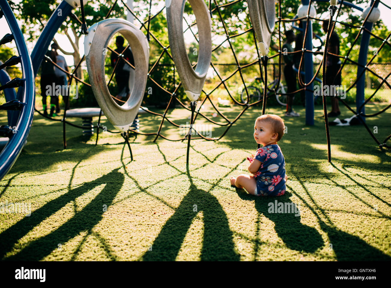 Baby girl sitting in beautiful light and shadows at a playground looking away. Stock Photo