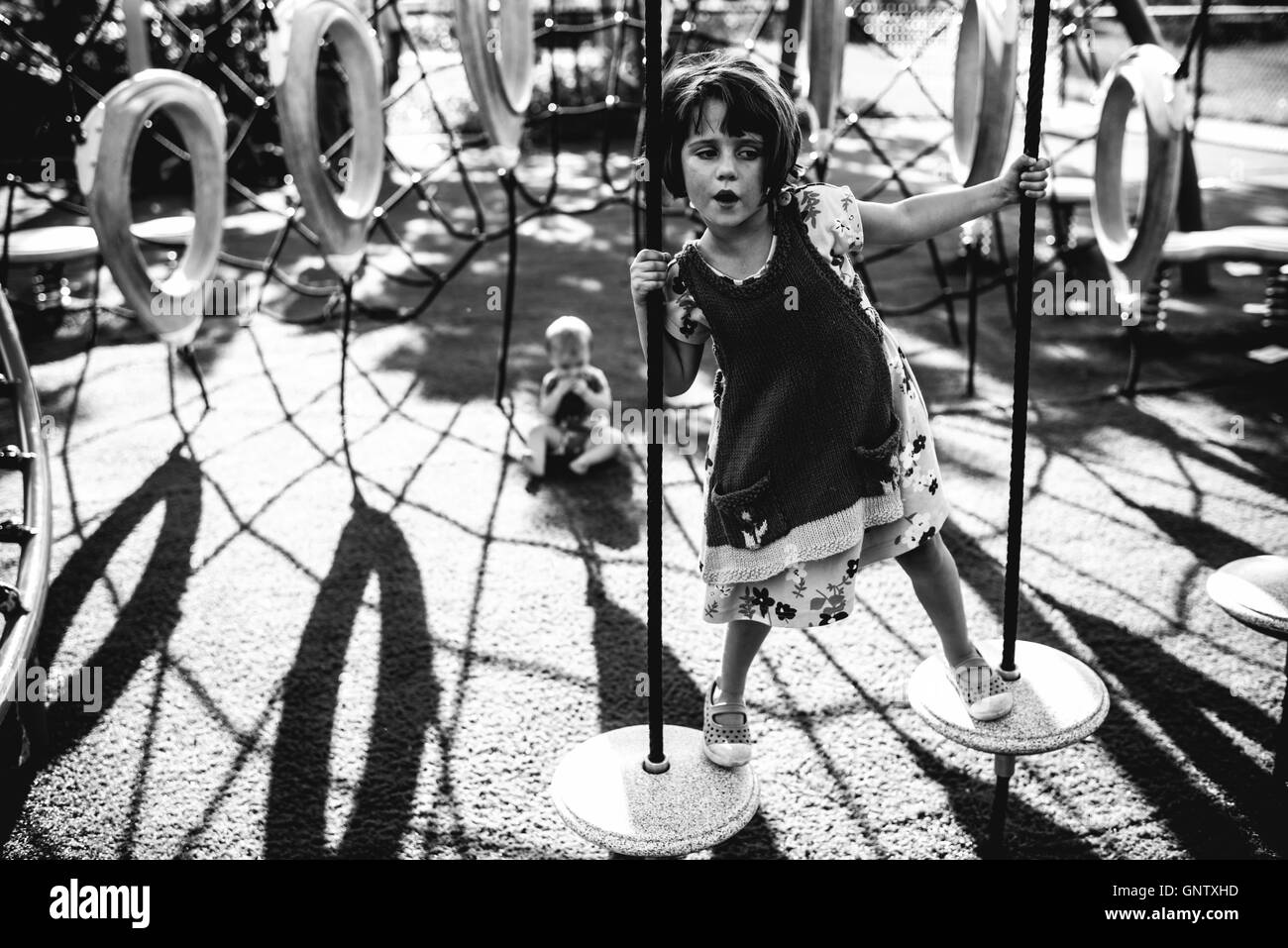 Little girl playing on playground with her baby sister in the background Stock Photo