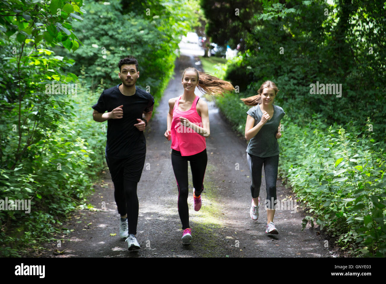 Three friends out running on forest trail, training and exercising. Fitness healthy lifestyle concept. Stock Photo