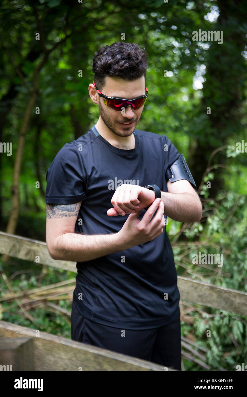 Man out running on forest trail, using his smart watch heart rate ...