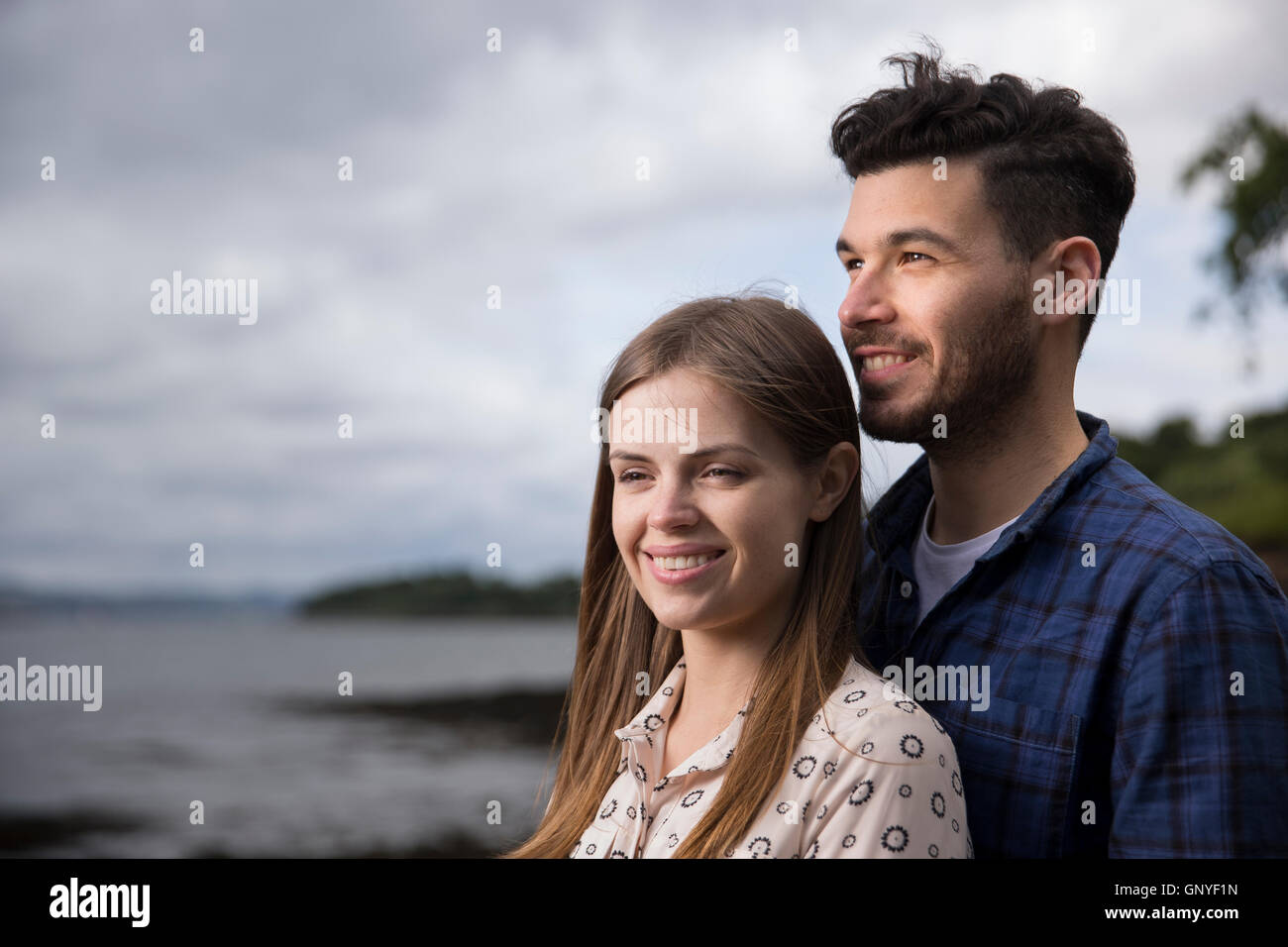 Relaxed young couple hugging while walking along pebble beach.  Caucasian lifestyle concept. Stock Photo