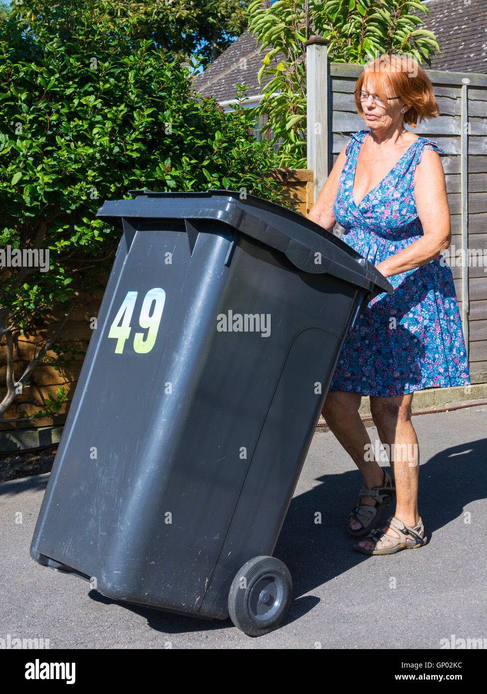 Middle aged lady taking out a rubbish bin. Stock Photo