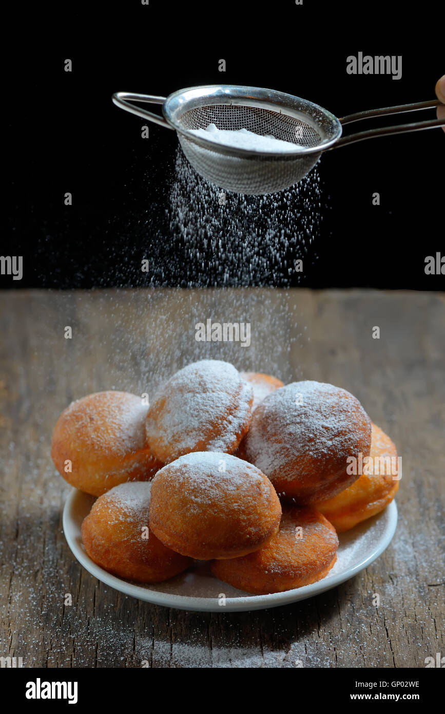 pours sugar with strainer over donuts Stock Photo