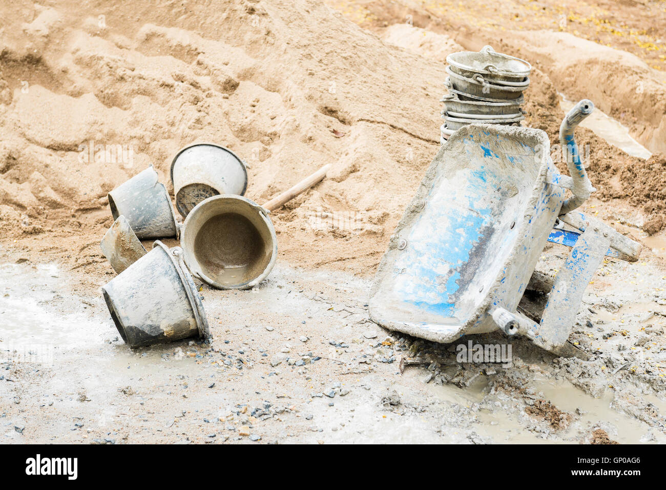 Blue sand barrow park lie on one side, bucket and sand pile beside at a construction site. Stock Photo