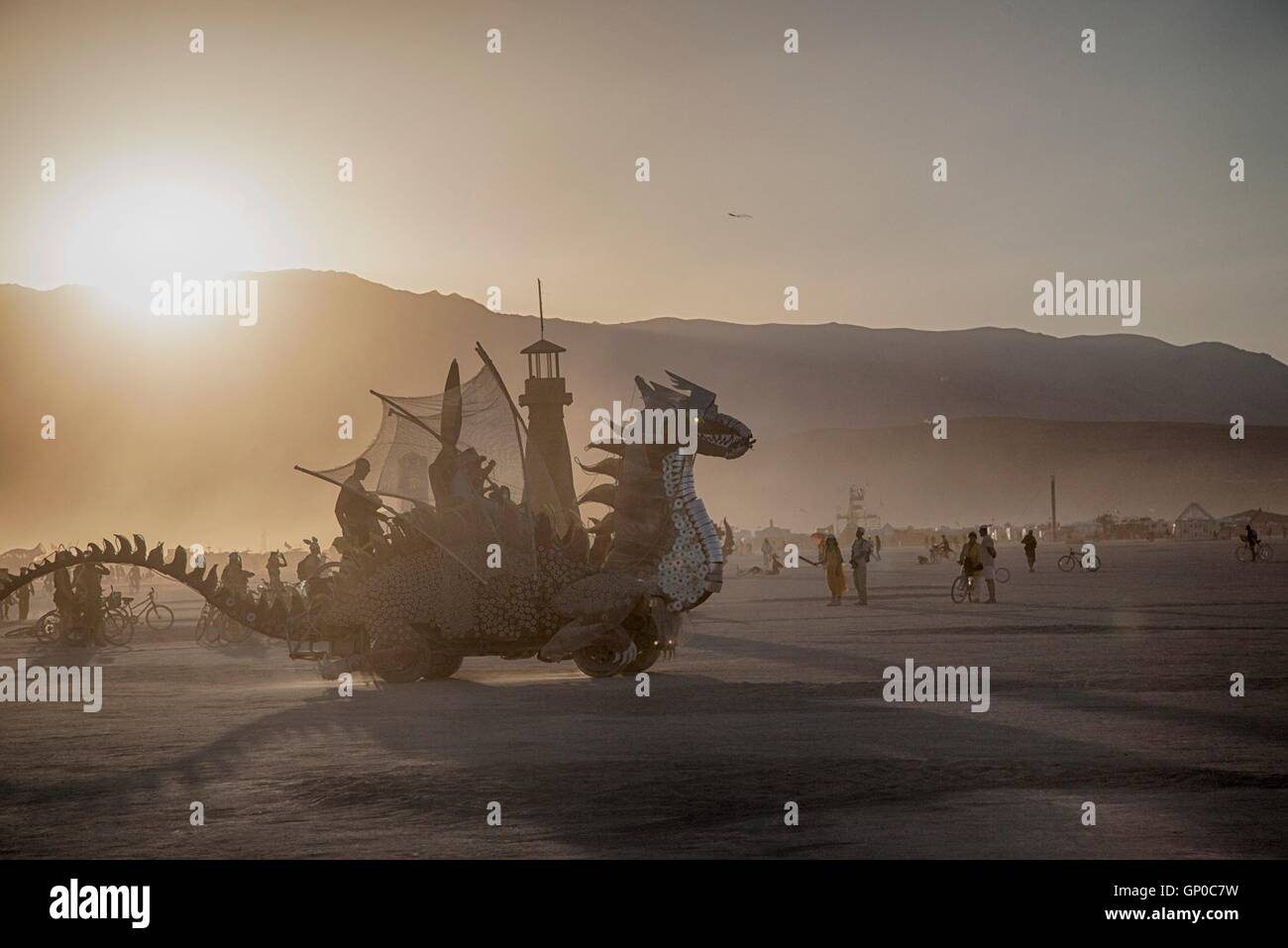 A dragon art car passes the Lighthouse art installation during a sunset dust storm at the annual desert festival Burning Man August 30, 2016 in Black Rock City, Nevada. The annual festival attracts 70,000 attendees in one of the most remote and inhospitable deserts in America. Stock Photo