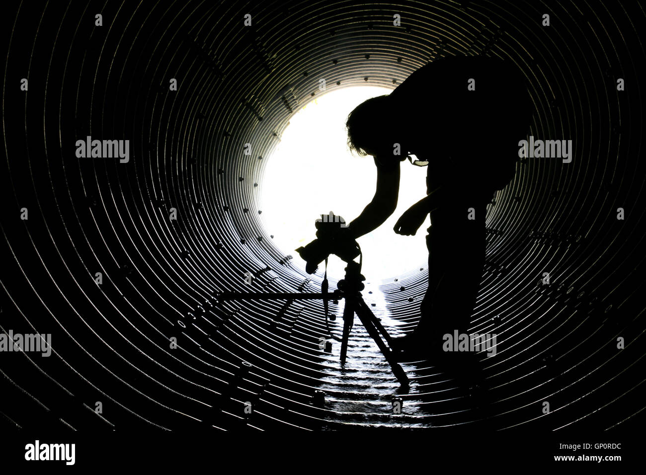 'Into the tunnel of photography', a silhouette of a photographer in a drainage tunnel Stock Photo
