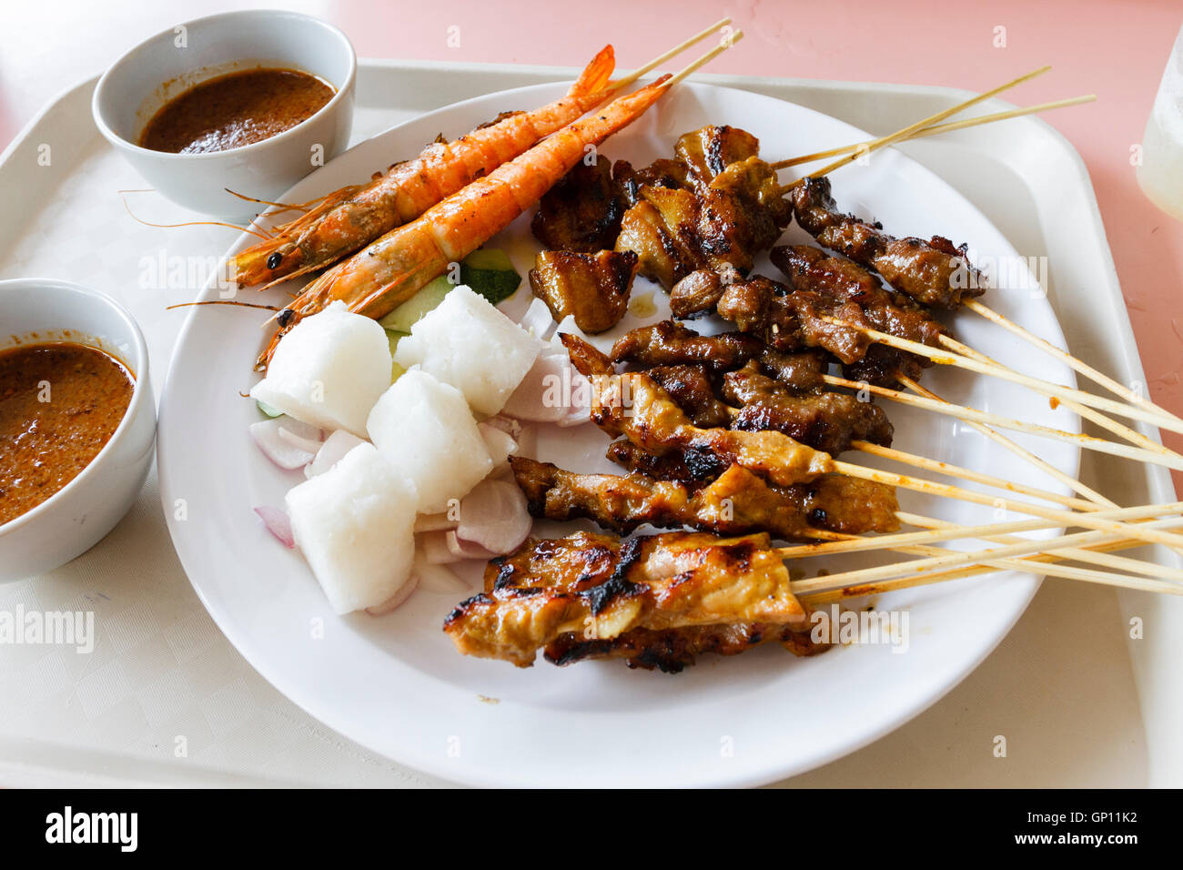 Plate of mixed satay food on a plate with bowls of satay sauce