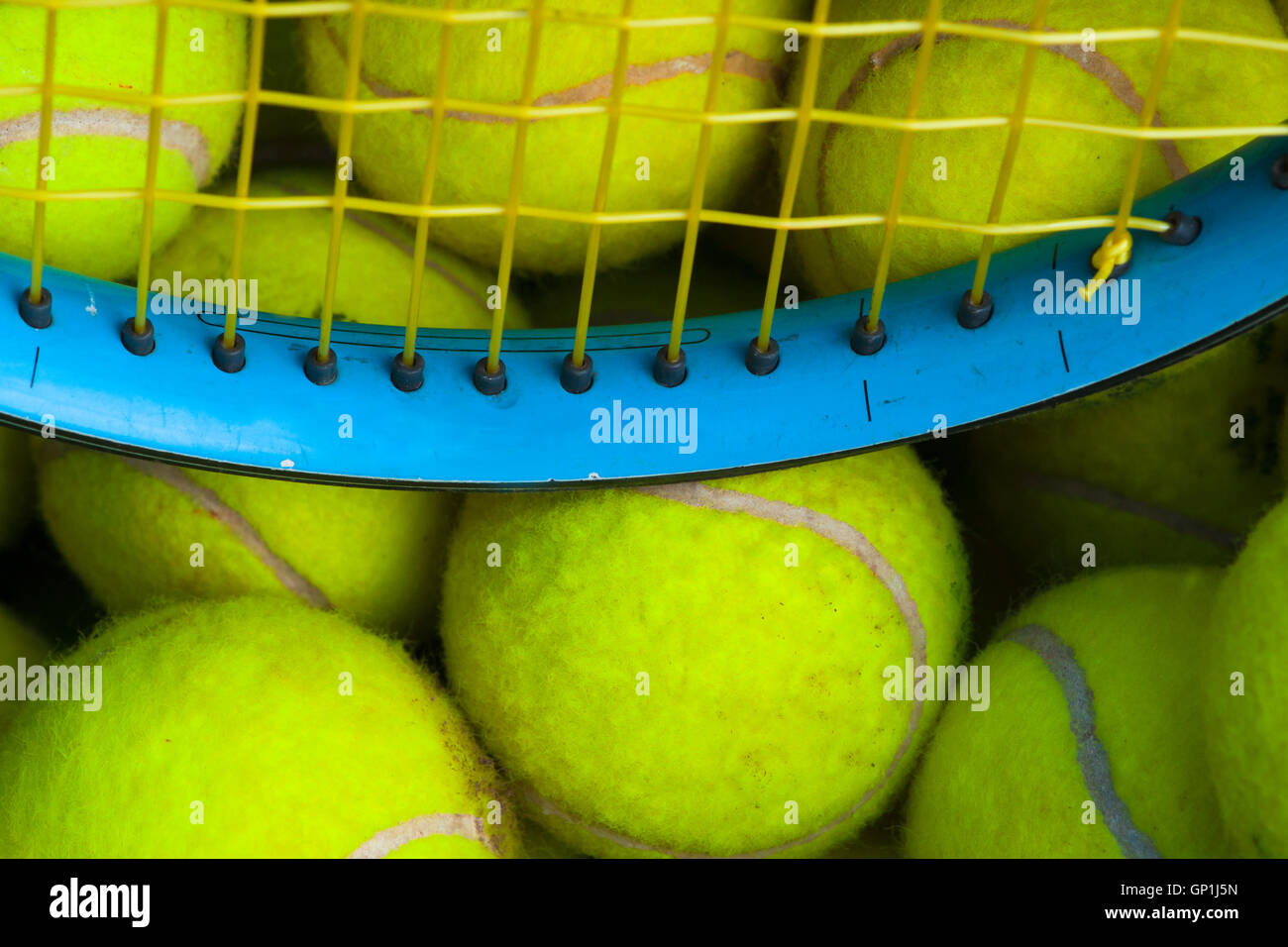A pile of light-green tennis balls and a tennis-racket in a box. Partial view of the racket. Court tennis theme. Stock Photo