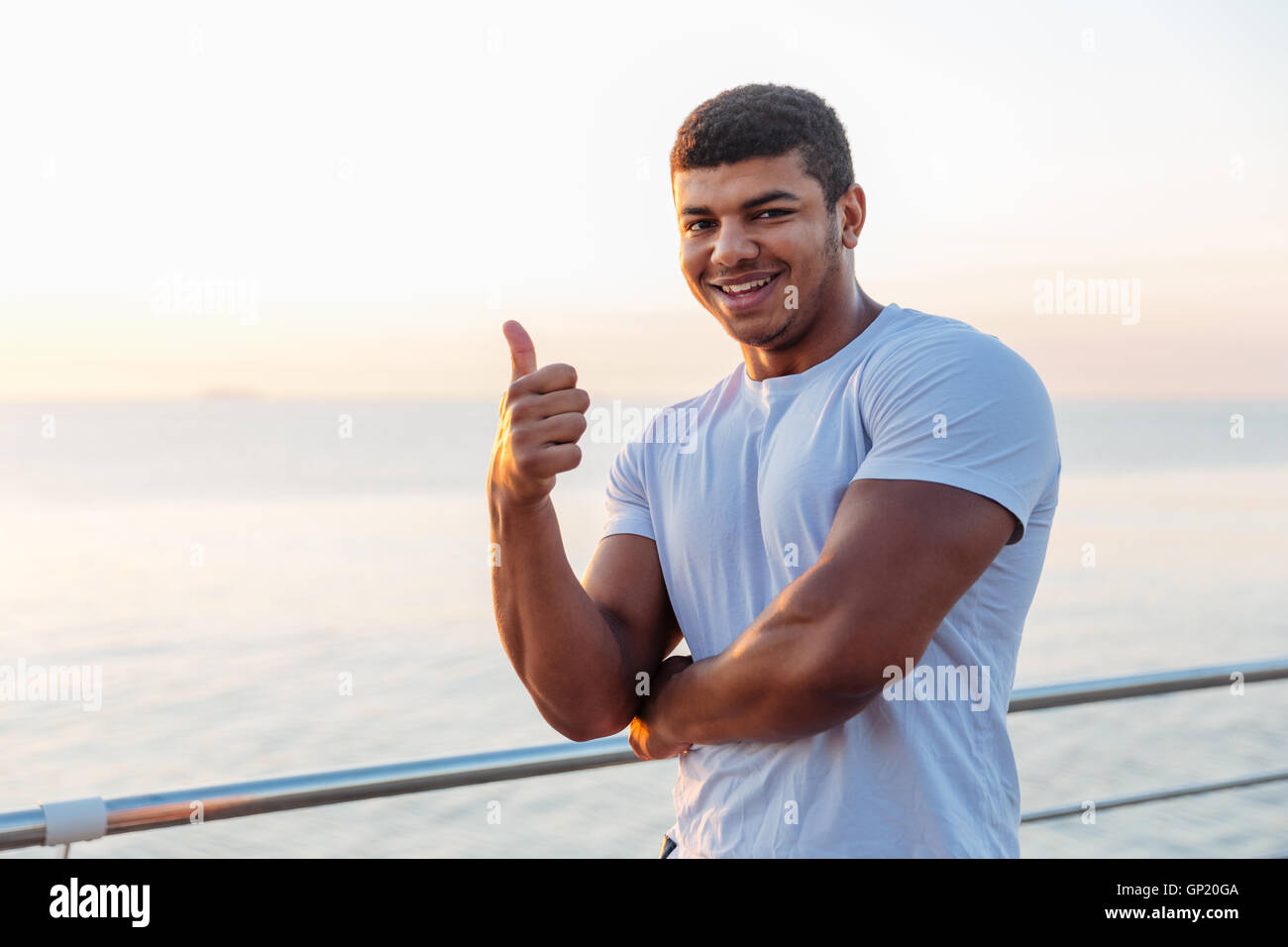 Cheerful african american young man athlete standing and showing thumbs up outdoors Stock Photo