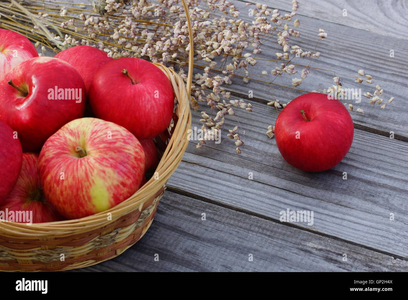 Basket with apples on a wooden table. Seasonal grass in the background. Stock Photo