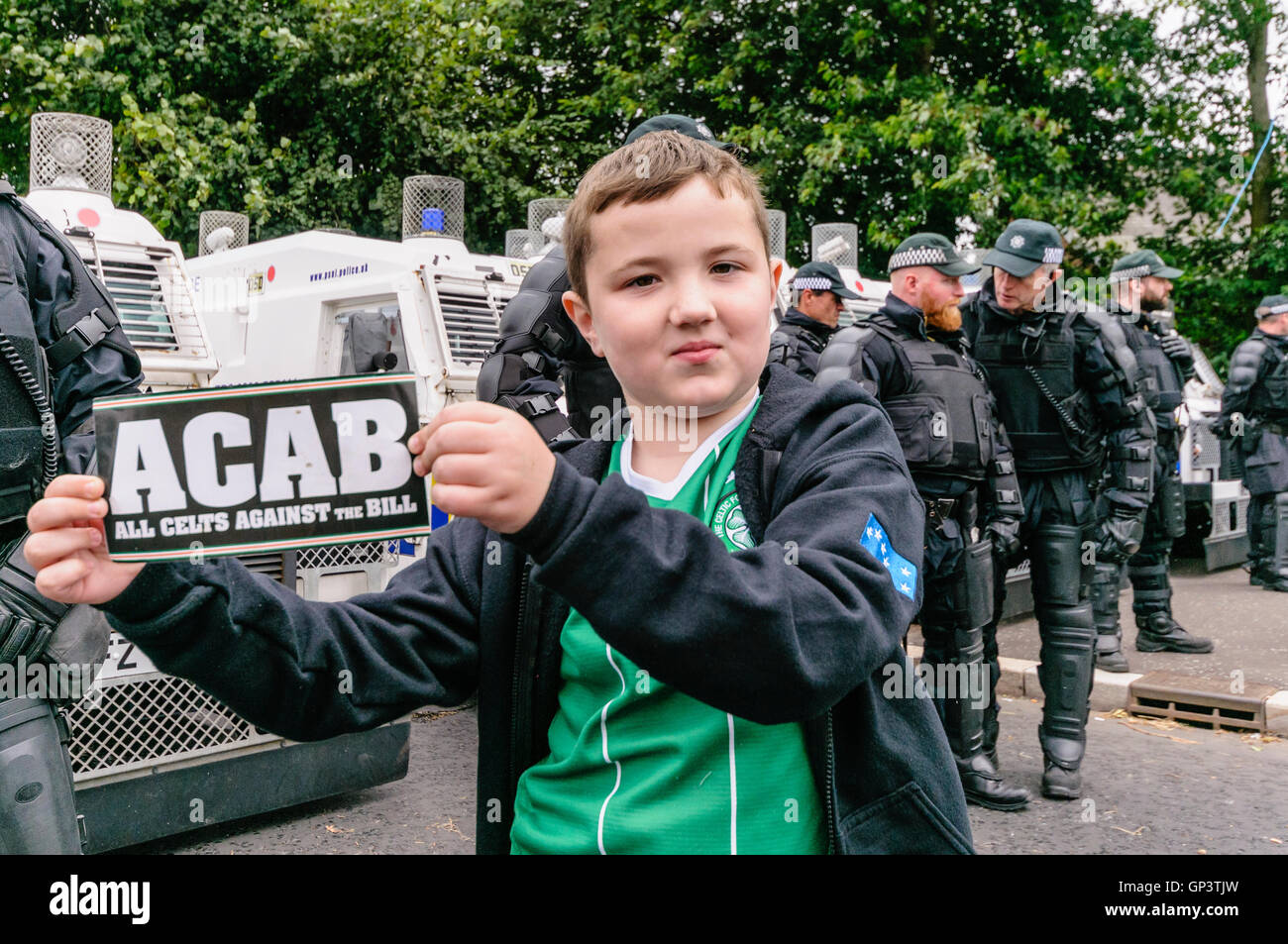 A young boy stands in front of a line of PSNI police officers, and holds a sign saying 'ACAB', claiming it stands for 'All Celts Against the Bill'.   ACAB is normally an acronym for 'All Cops Are Bastards'. Stock Photo