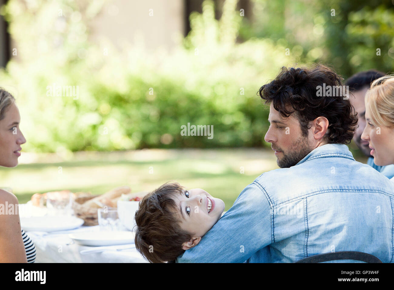 Family together at outdoor table, boy smiling over his shoulder Stock Photo