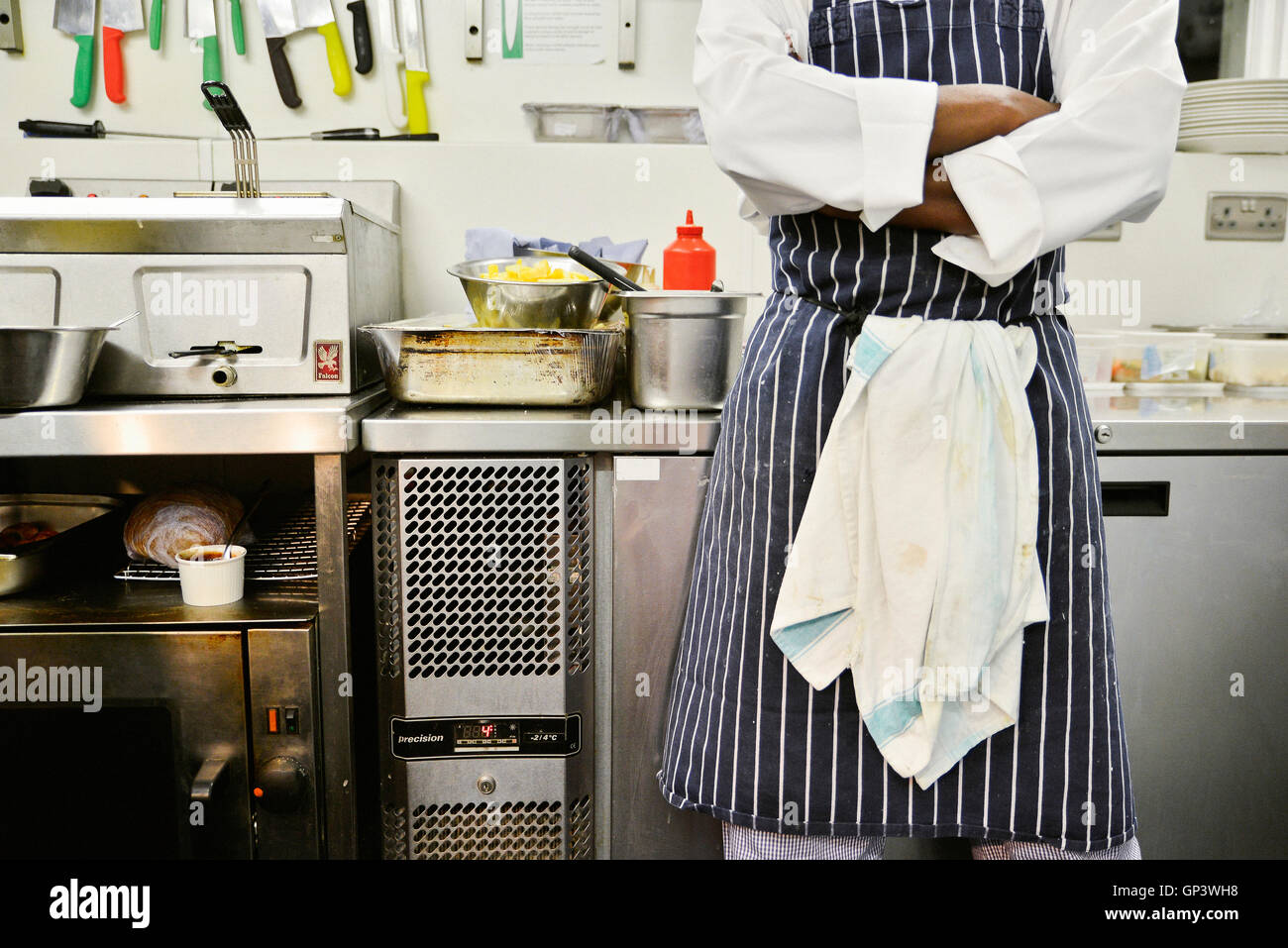 Chef standing in commercial kitchen with arms folded, mid section Stock Photo