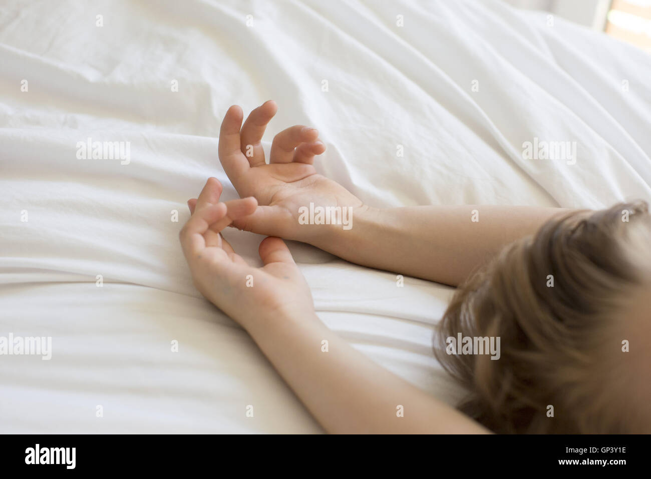 Boy relaxing on bed with arms above head, cropped Stock Photo