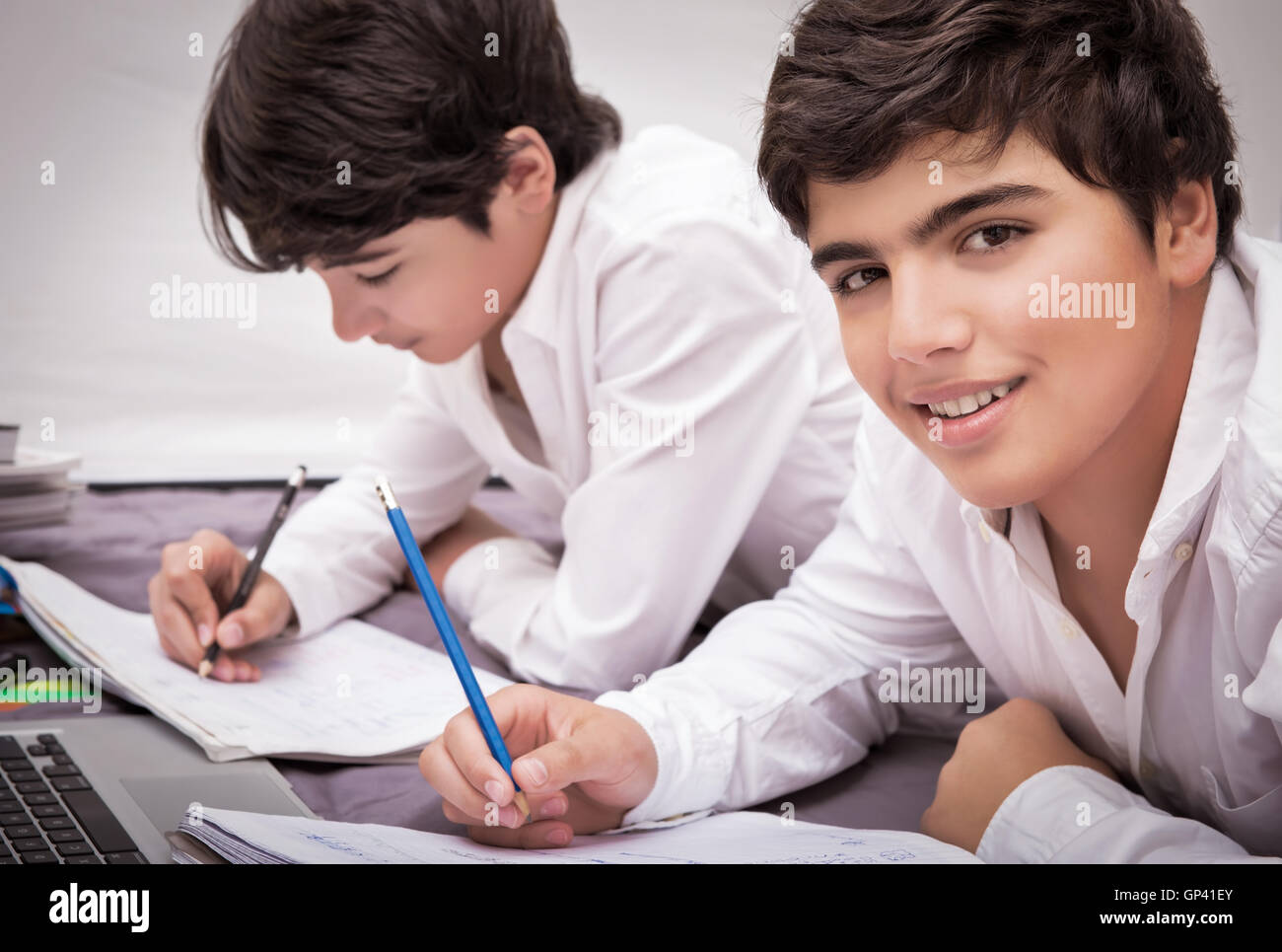 Two teenage boys doing homework at home, writing something in their notebooks, enjoying at school, education concept Stock Photo