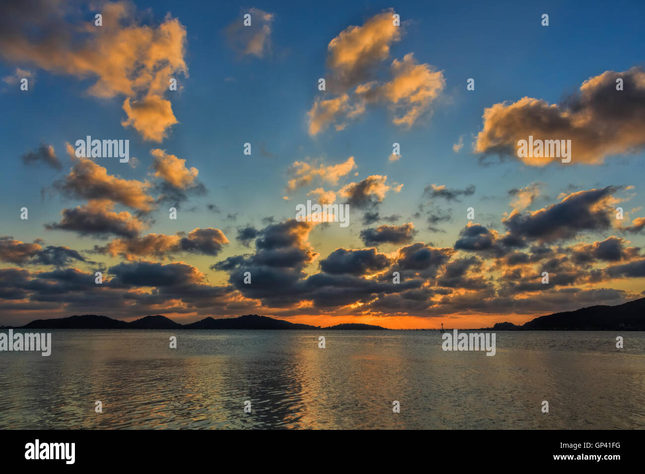 Partly cloudy sunset mountain reflections sea colors. Stock Photo