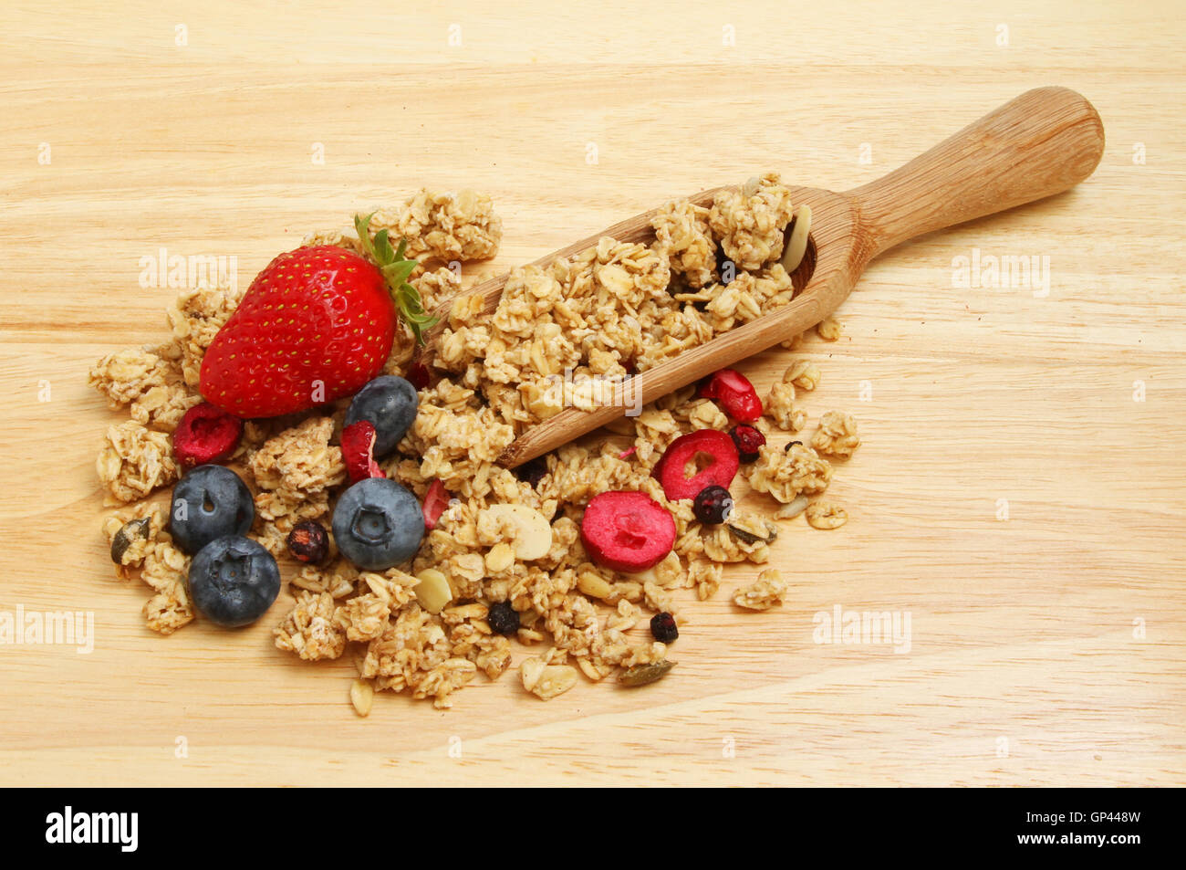 Granola with fresh strawberries and blueberries in a wooden scoop on a chopping board Stock Photo