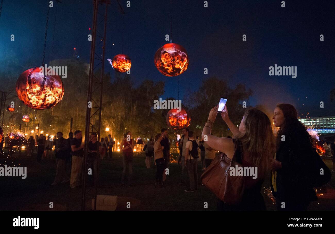 People photograph a burning structures as a part of 'Fire Garden' by Compagnie Carabosse, in front of the Tate Modern in London to mark the 350th anniversary of the Great Fire of London. Stock Photo