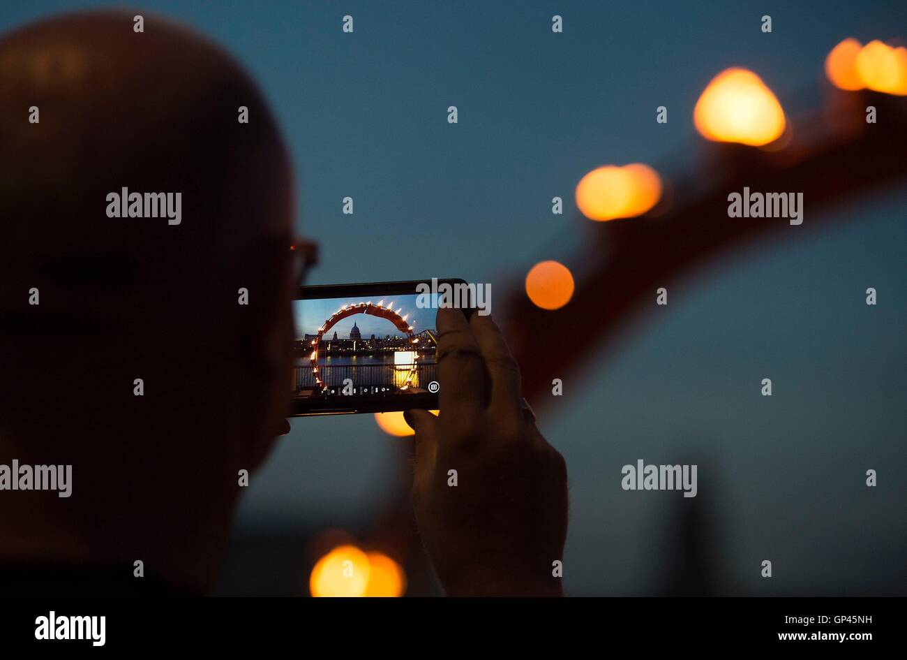 A man photographs a burning structure as part of 'Fire Garden' by Compagnie Carabosse, in front of the Tate Modern in London to mark the 350th anniversary of the Great Fire of London. Stock Photo