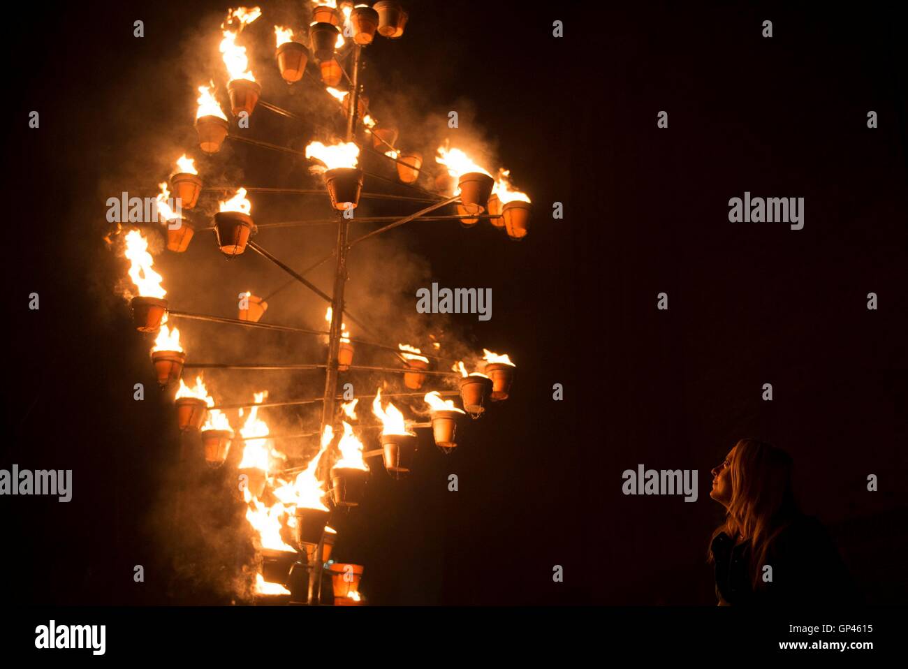 A woman looks at a burning structure as part of 'Fire Garden' by Compagnie Carabosse, in front of the Tate Modern in London to mark the 350th anniversary of the Great Fire of London. Stock Photo