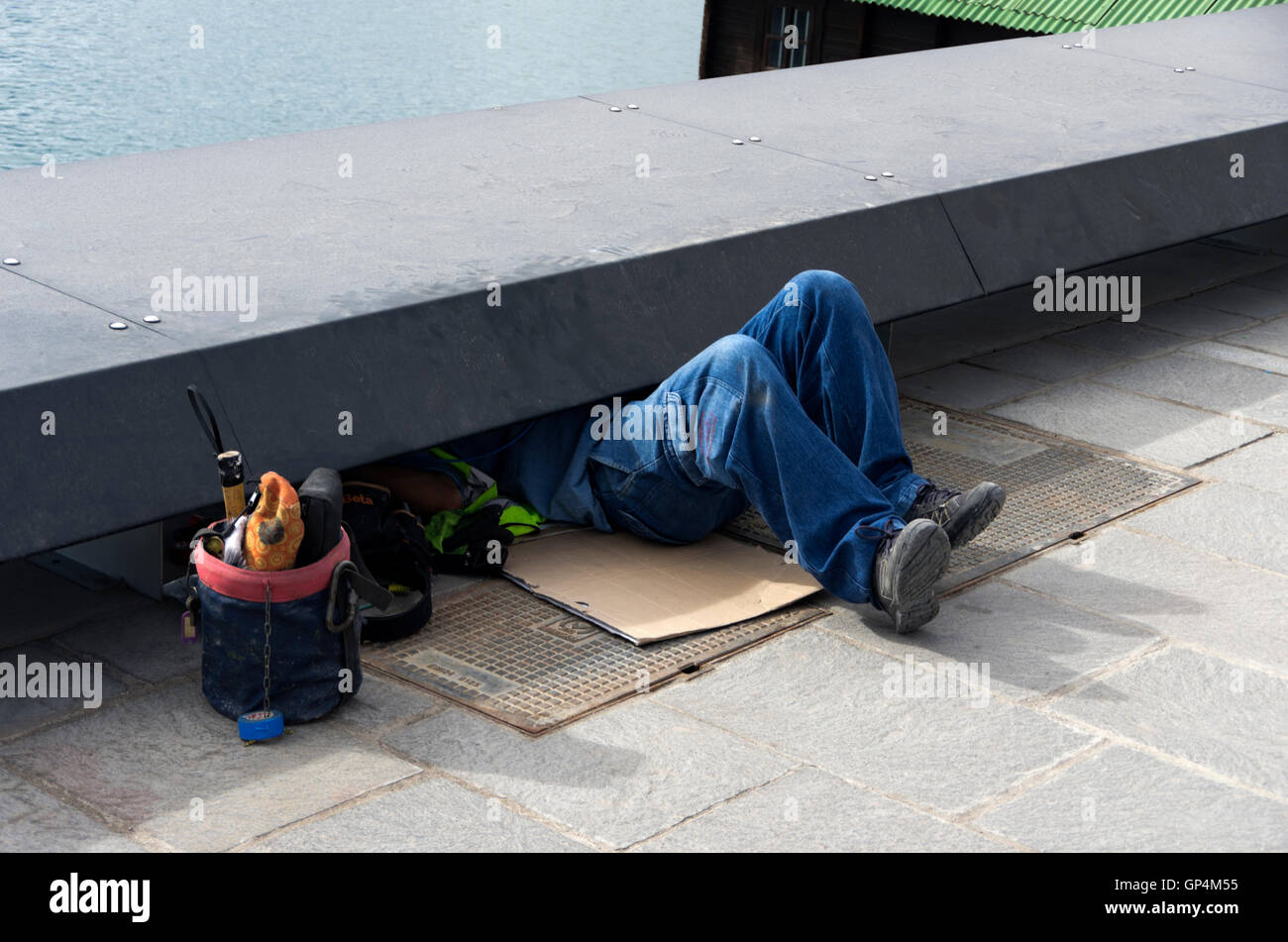 Legs stick out from under sidewalk, as workman works underneath. Stock Photo