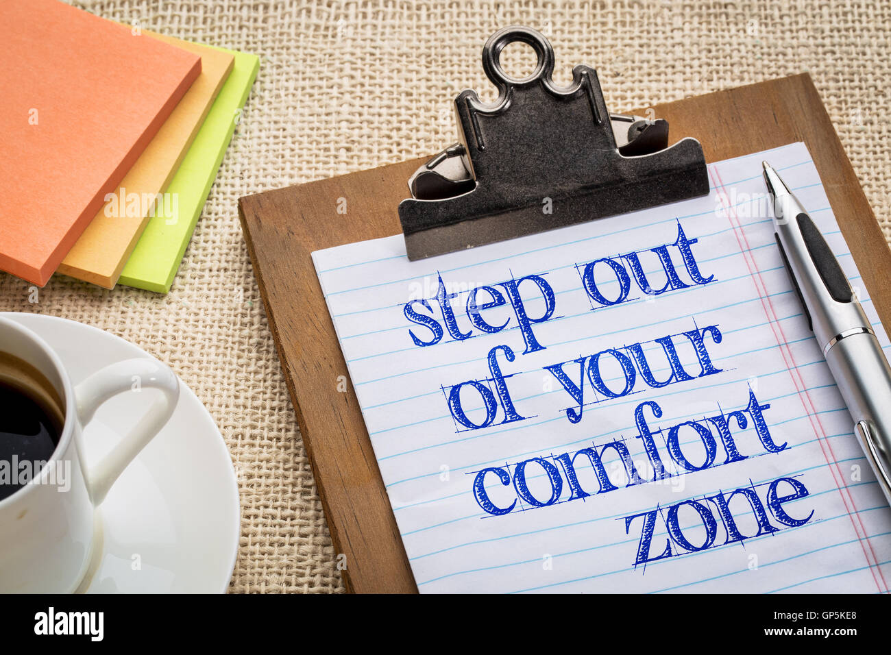 Step out of your comfort zone text on clipboard  with a pen, coffee and sticky notes against burlap canvas - office abstract Stock Photo