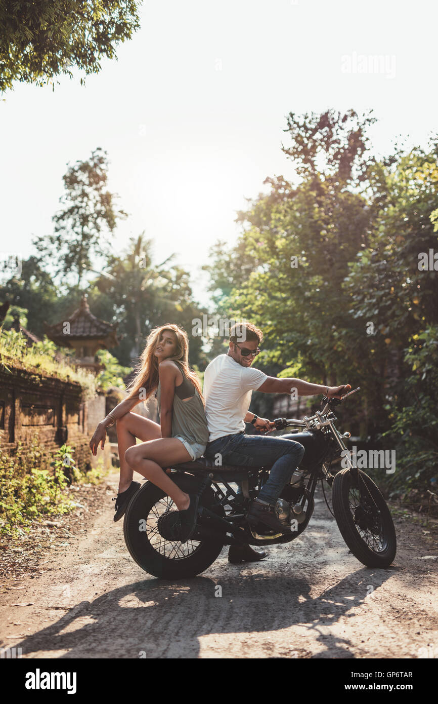 Outdoor shot of young couple hanging out with motorcycle on village road. Young man and woman on motorbike. Stock Photo