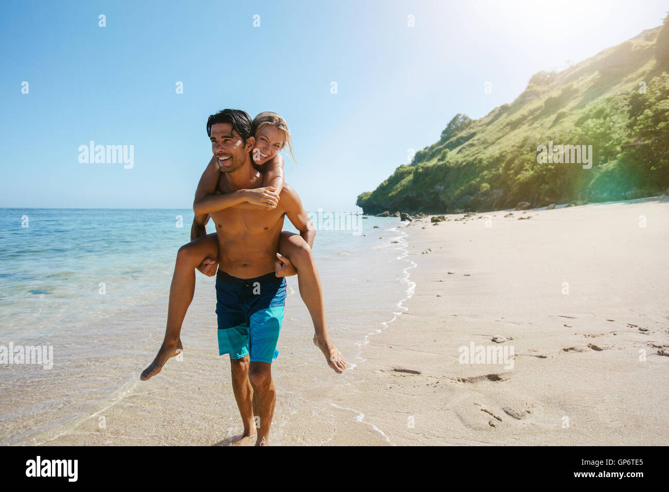 Happy couple in love on beach summer vacations. Joyful woman piggybacking on boyfriend, playing and having fun on travel vacatio Stock Photo