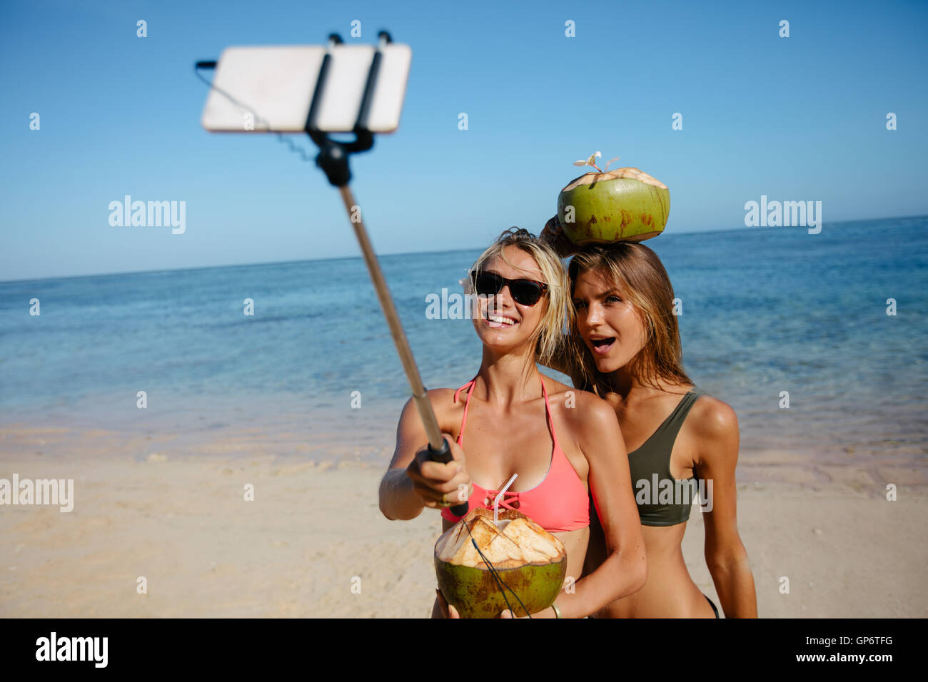 Two young women taking picture with smartphone on selfie stick on beach. Female friends in bikini enjoying summer holidays on th Stock Photo